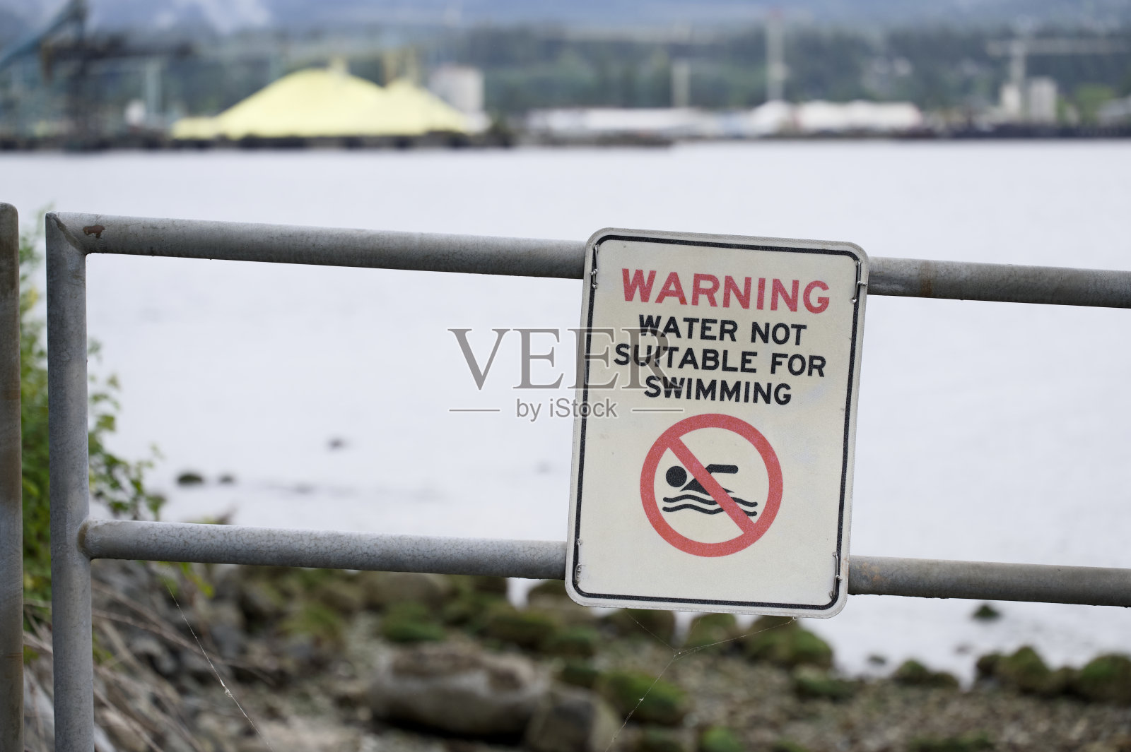 栏杆上挂着以工业为背景的警告水域不宜游泳的标志照片摄影图片