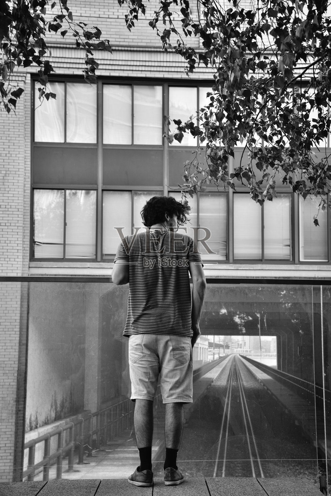 一个年轻人站在高线公园上，透过玻璃栏杆向外看，背景是建筑正面的火车轨道图像照片摄影图片