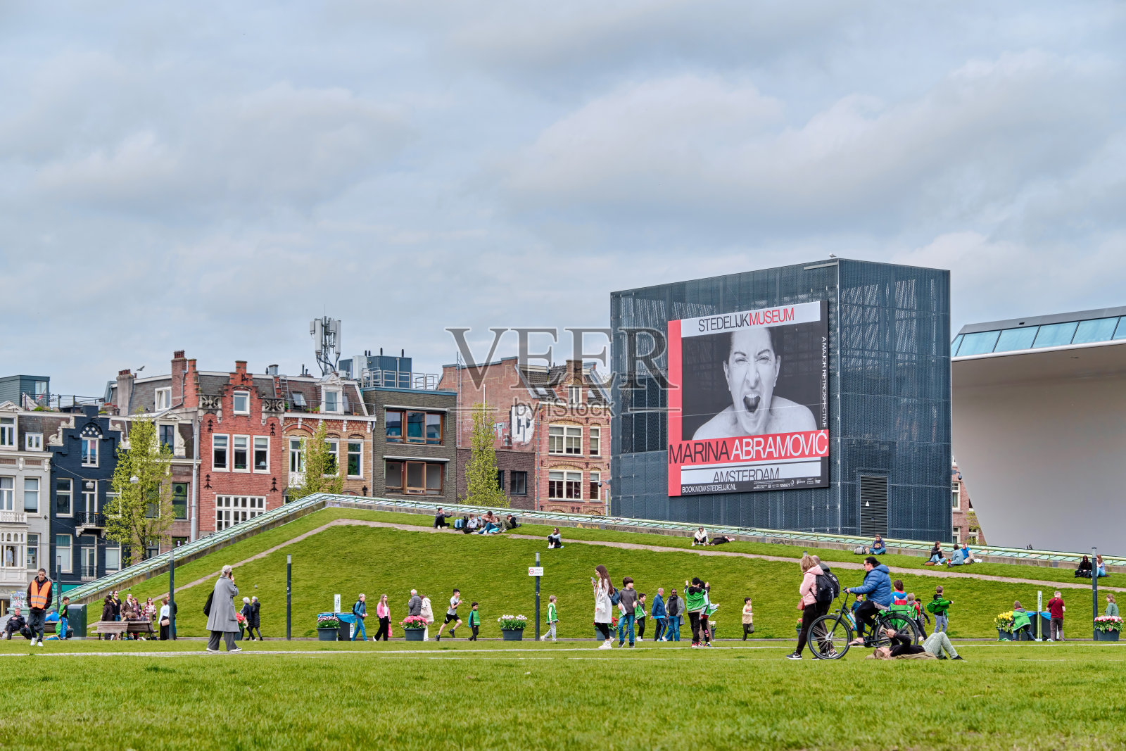 图为，人们在阿姆斯特丹市立博物馆和阿布拉莫维奇海报前的博物馆广场散步和休息照片摄影图片