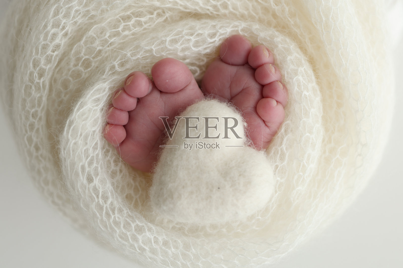 新生婴儿的小脚。新生儿柔软的脚裹在白色的羊毛毯子里。新生儿的脚趾、脚跟和脚的近照。在婴儿的腿上编织白色的心。微距摄影照片摄影图片