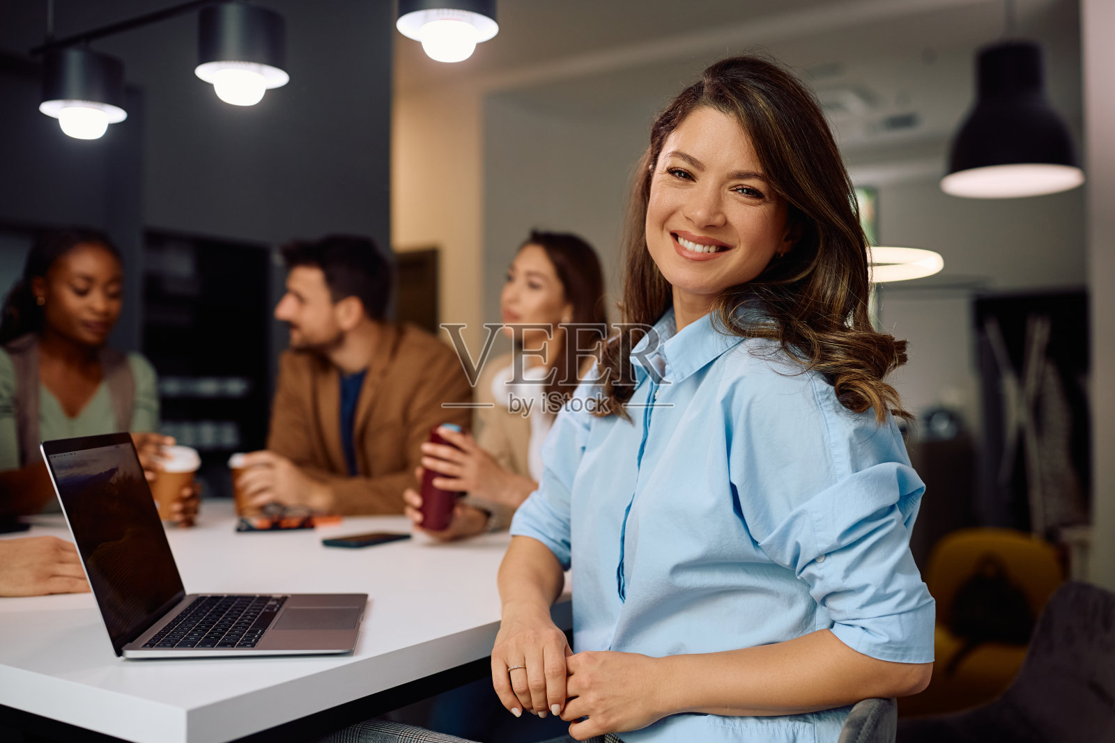 快乐的企业家在和同事喝咖啡休息时使用笔记本电脑，看着相机。照片摄影图片