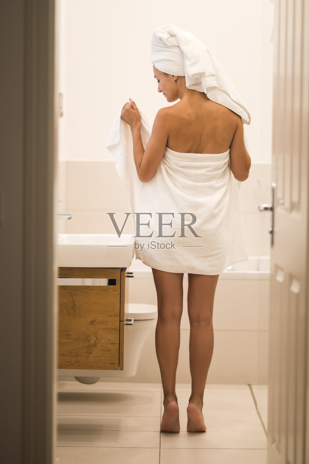 穿着白毛巾的苗条年轻女子站在浴室里照片摄影图片