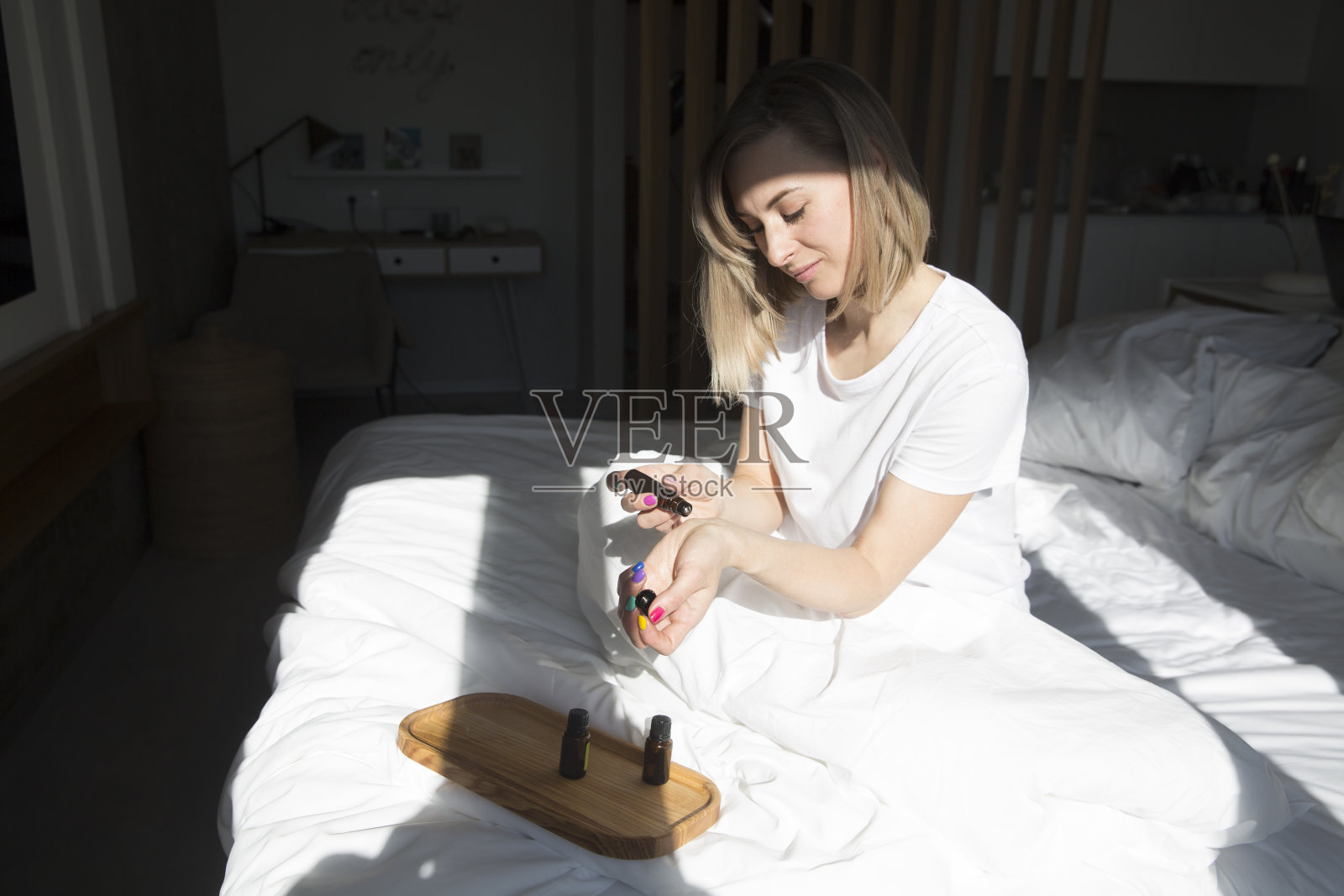 女人早晨坐在床上用精油，享受香味。芳香疗法照片摄影图片