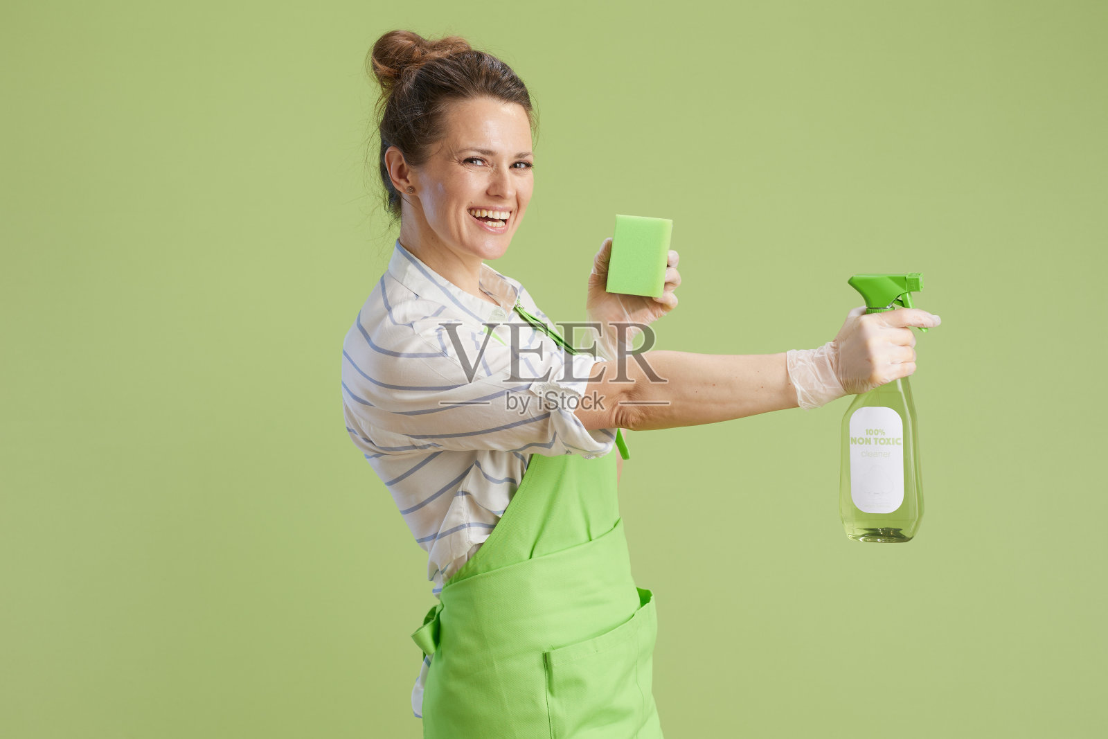 微笑的女人穿着绿色的围裙，戴着绿色的橡胶手套照片摄影图片