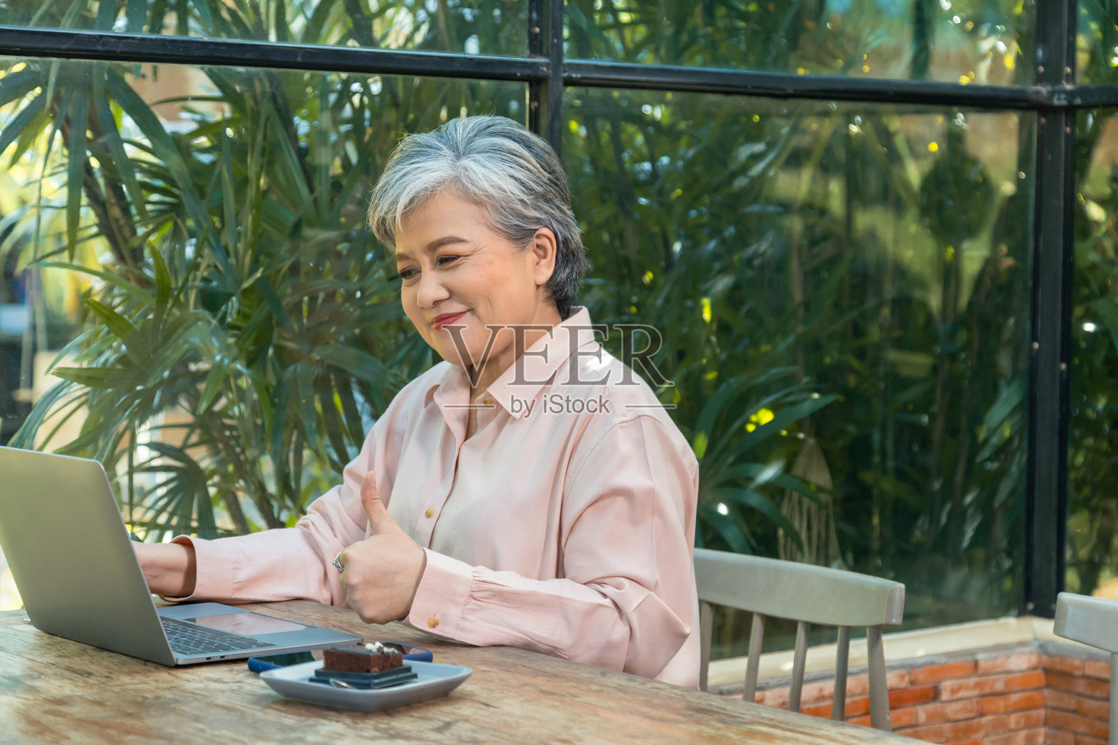 老年女性坐在咖啡馆里喝着葡萄酒，拿着科技笔记本电脑，亚洲60多岁的老人退休后开心地看电影或与朋友聊天。能力老年人工作照片摄影图片