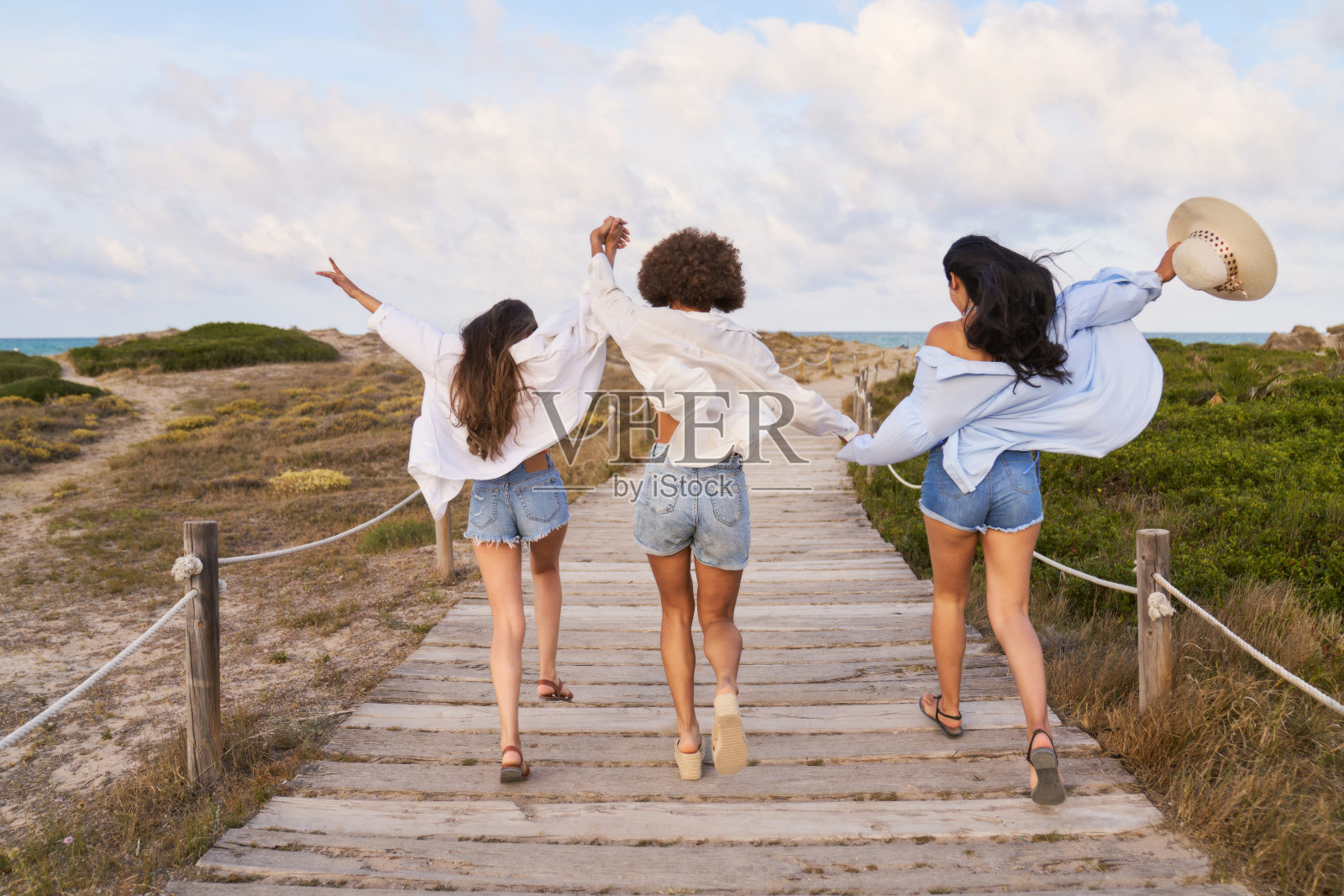 三个女人在一条木板路上跑步，其中一个戴着帽子照片摄影图片