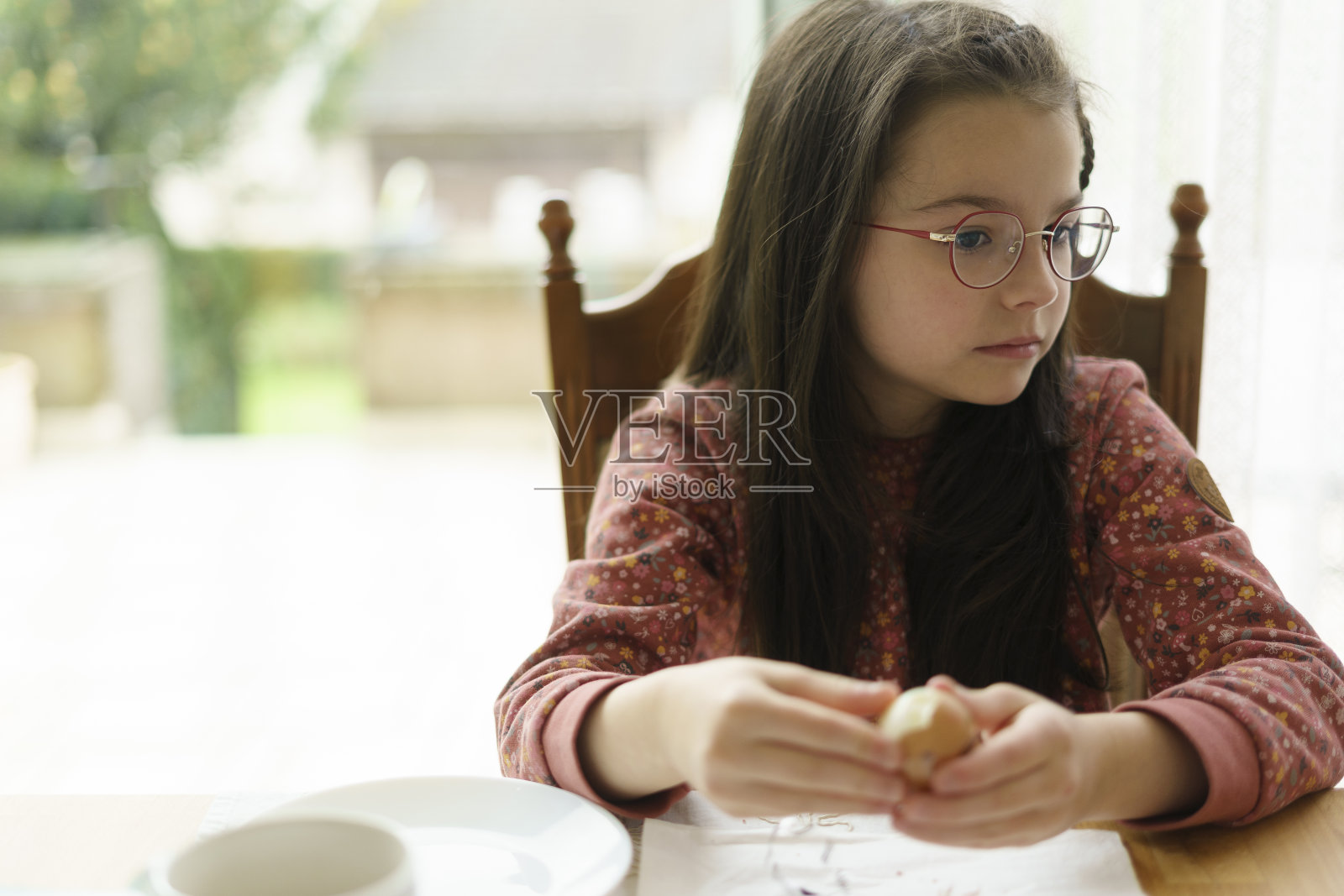 一个戴眼镜的漂亮小女孩坐在桌子旁，正在清洗复活节彩蛋。照片摄影图片