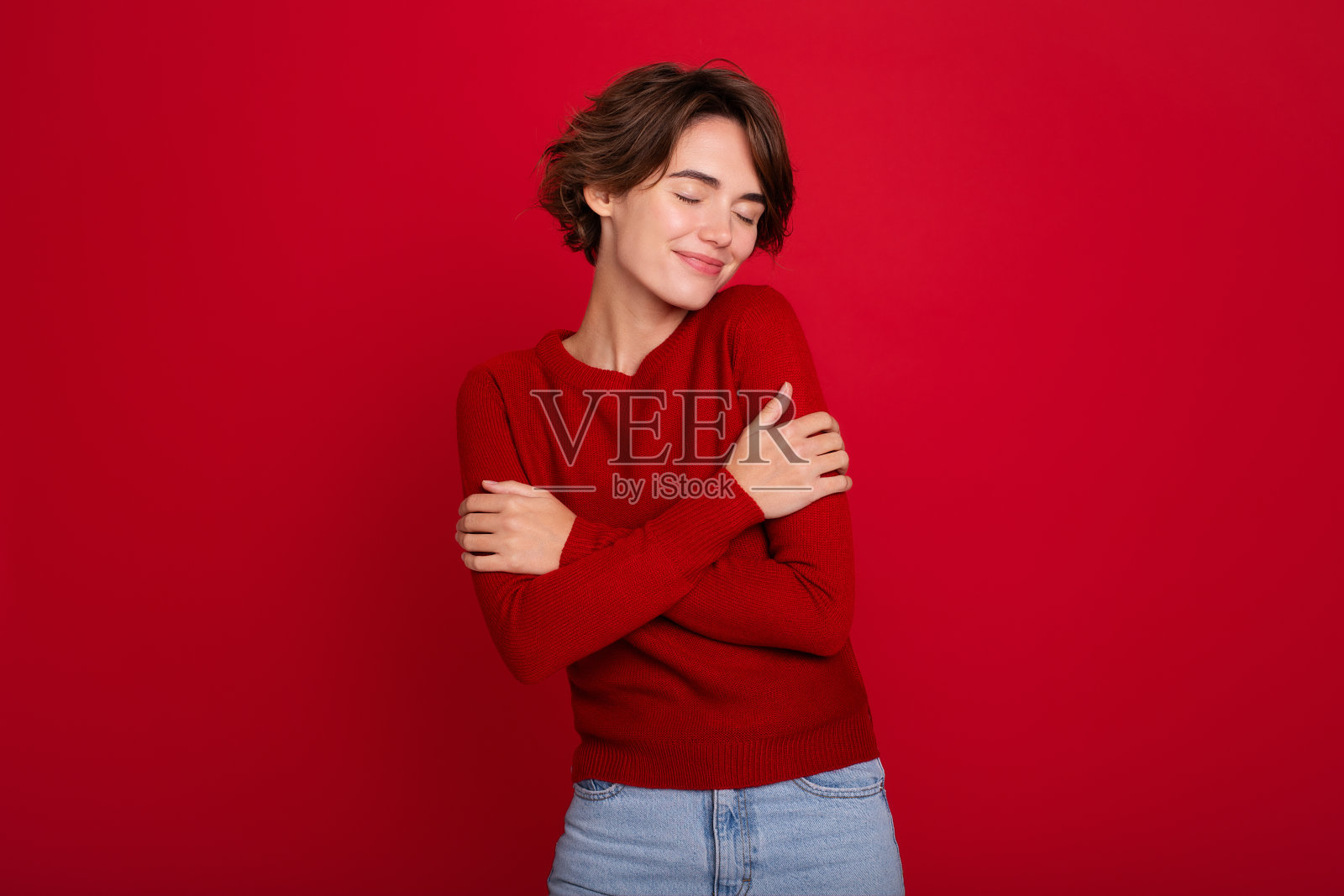 可爱，可爱，温柔的年轻女孩穿着红色毛衣，闭着眼睛在红色的墙上摆姿势照片摄影图片