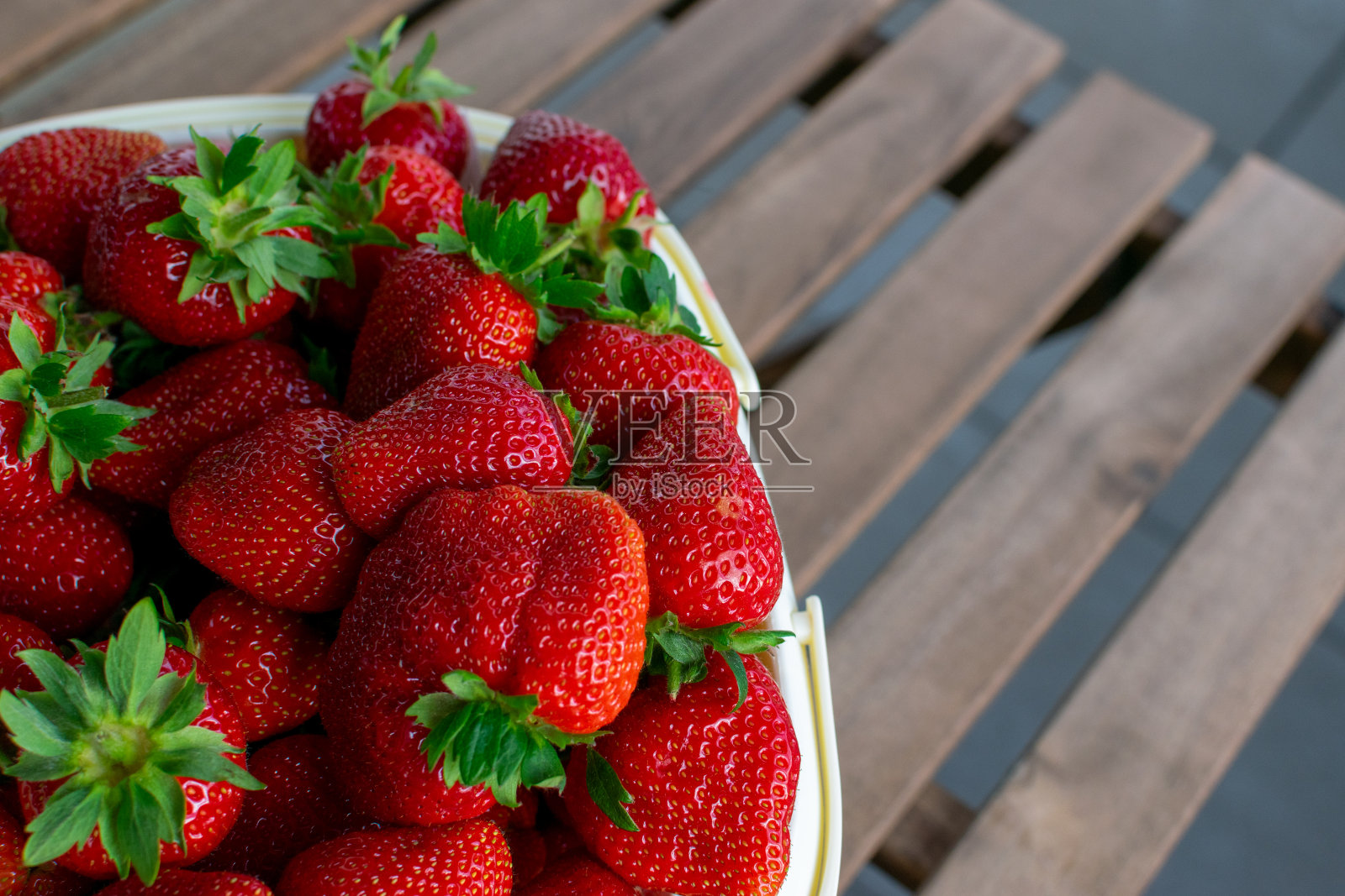 木桌上一篮新鲜的红草莓的特写。照片摄影图片