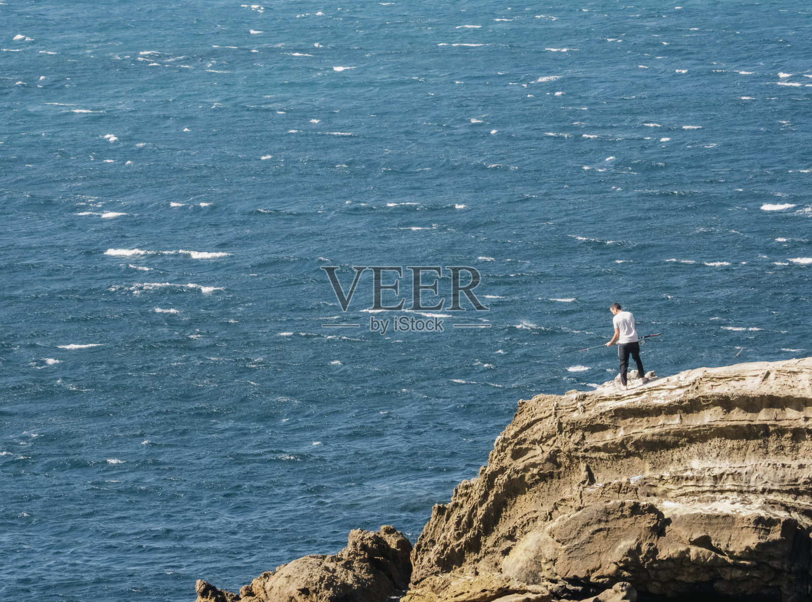 一个人把钓鱼竿扔在海边的岩石上照片摄影图片