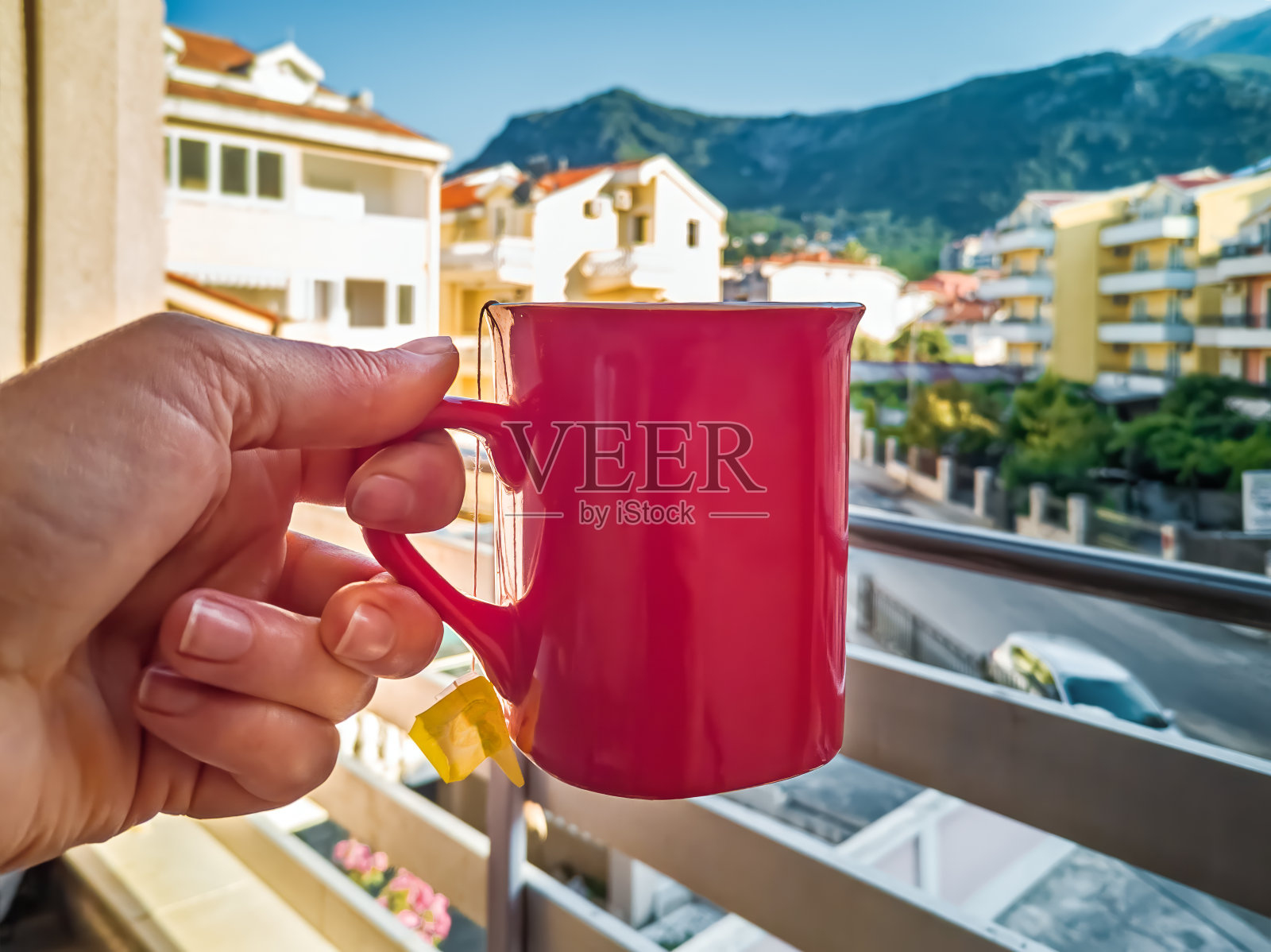 一位女士手捧着一杯红色的茶，背景是黑山布德瓦市模糊的城市景观照片摄影图片
