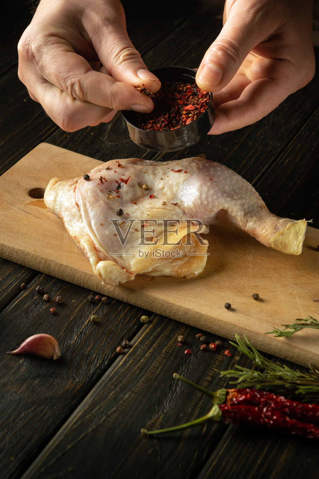 厨师在烤鸡腿之前先用香料调味。工作环境在厨房桌子上放胡椒和迷迭香照片摄影图片
