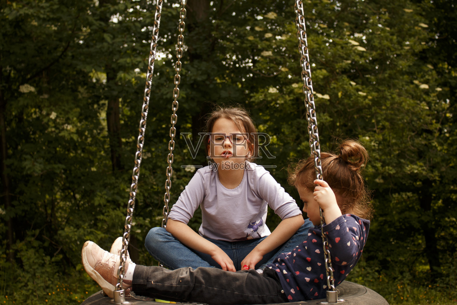 两个小姐妹一起在公园里荡秋千。大自然中的家庭乐趣照片摄影图片