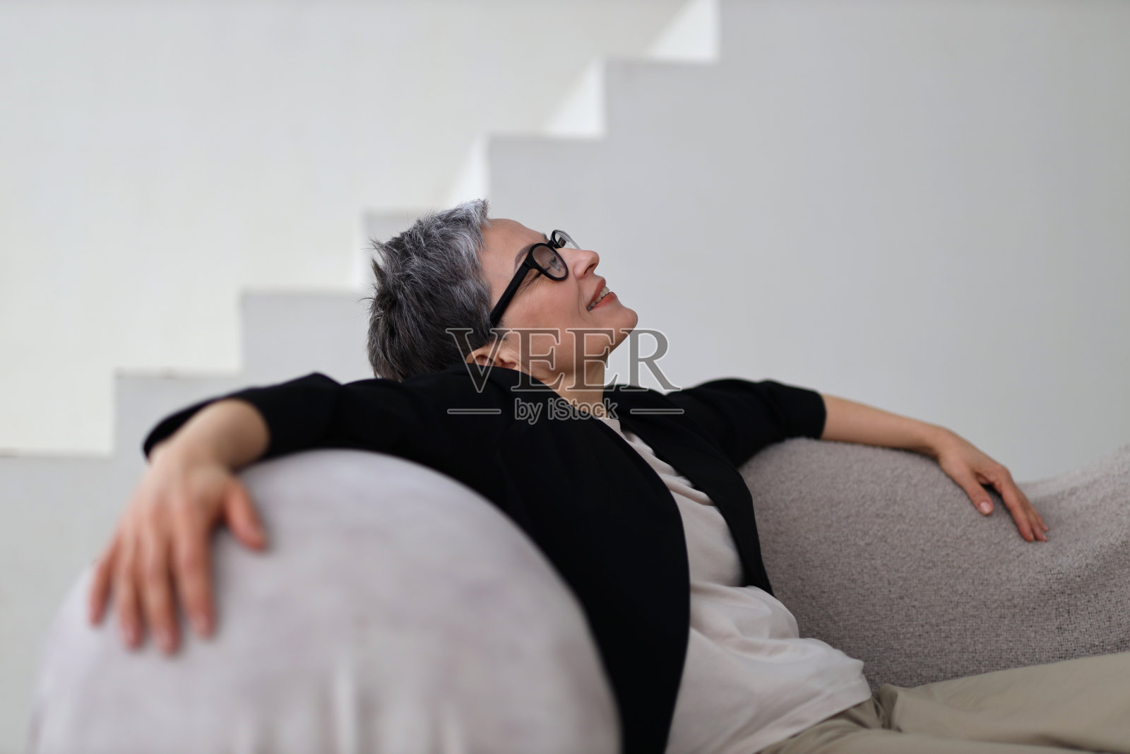 一个宁静的女人享受着一个宁静的周末，舒适地躺在沙发上，体现着平静和幸福。照片摄影图片