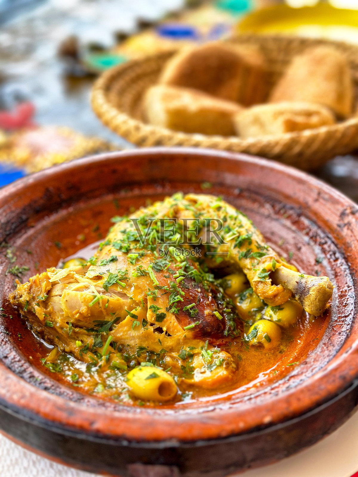 传统摩洛哥菜，加香料和卡拉马塔橄榄的炖鸡，背景是面包篮照片摄影图片