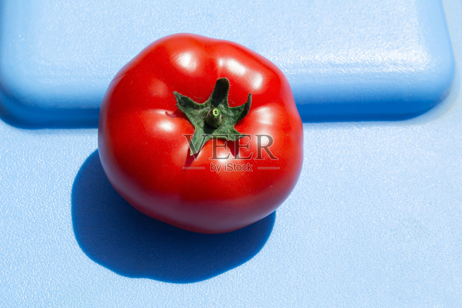 在抽象的蓝色背景上，用强光照射西红柿的照片，用于食品行业的时尚设计照片摄影图片