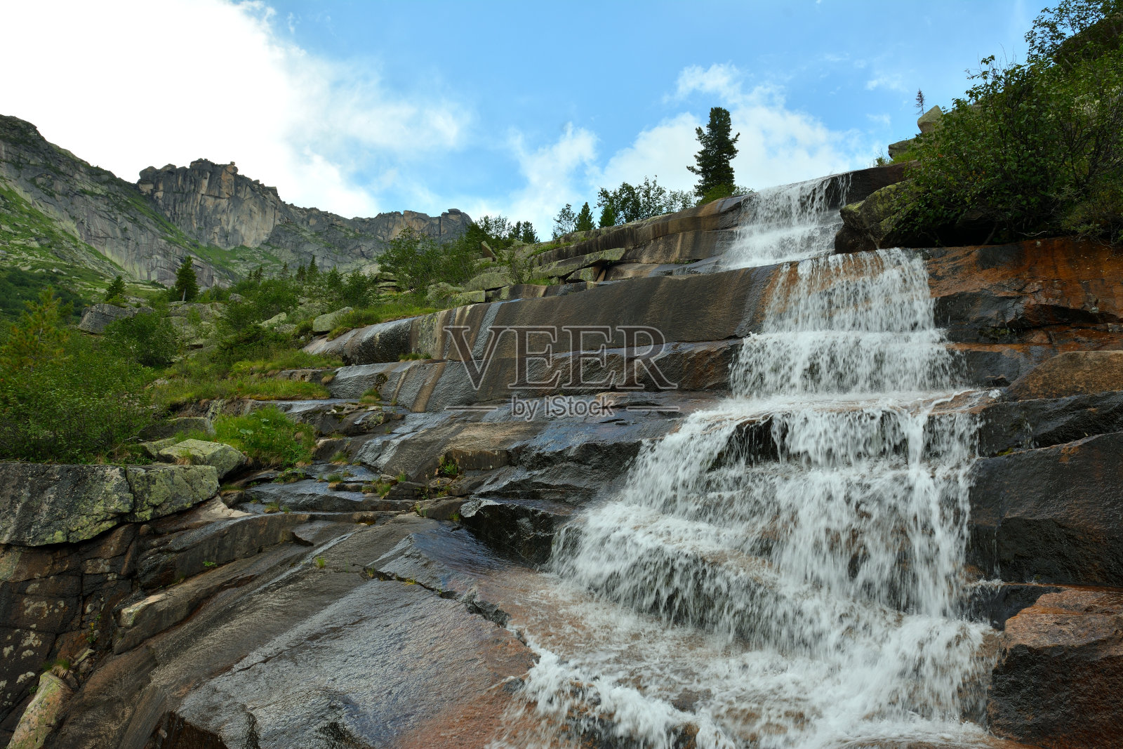 在一个多云的夏日里，石阶形式的高大岩石和瀑布般的山间河流形成瀑布。照片摄影图片