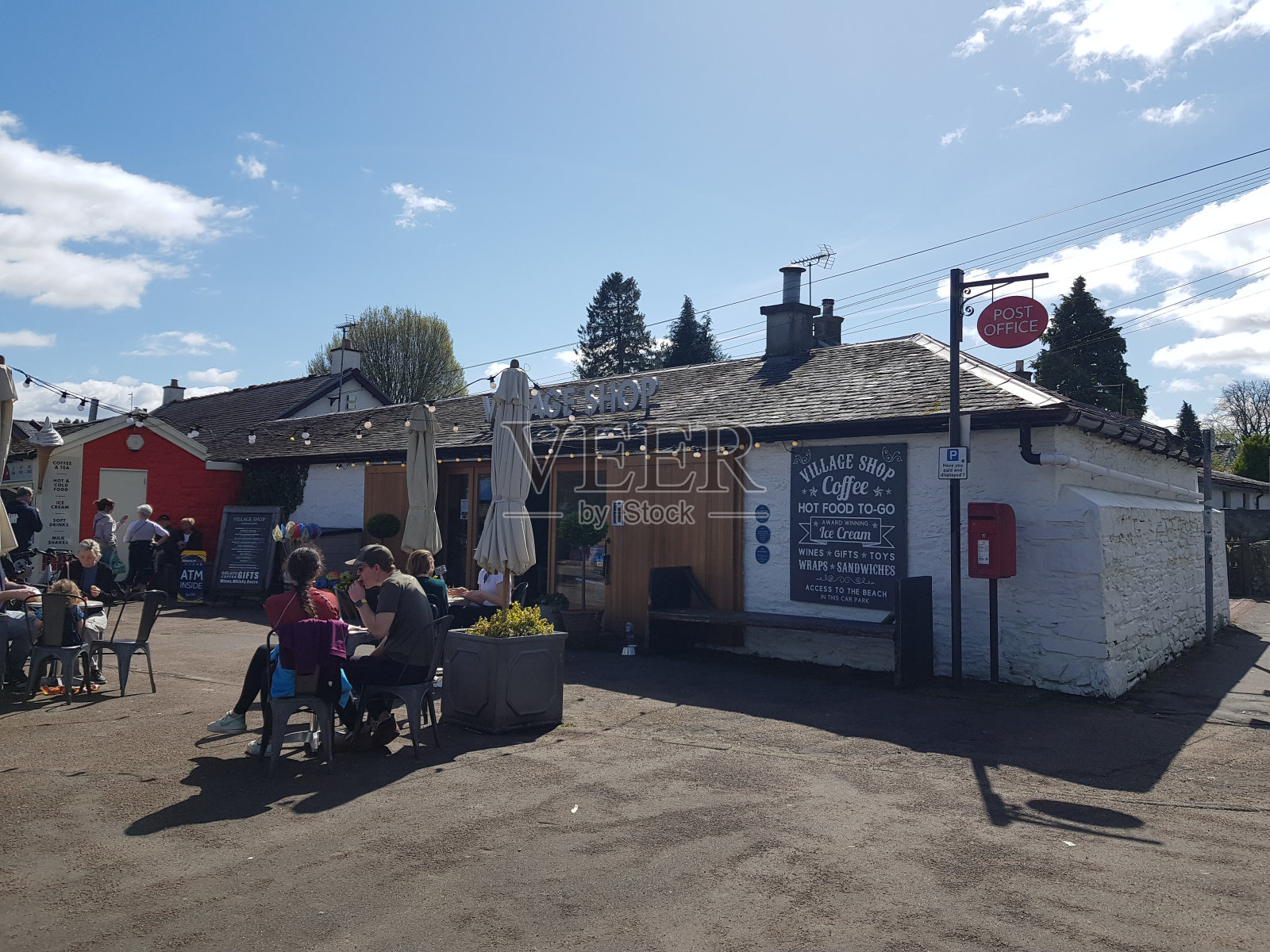 在一个阳光明媚的日子里,人们坐在英格兰苏格兰洛蒙德湖卢斯的一家乡村商店前吃东西照片摄影图片