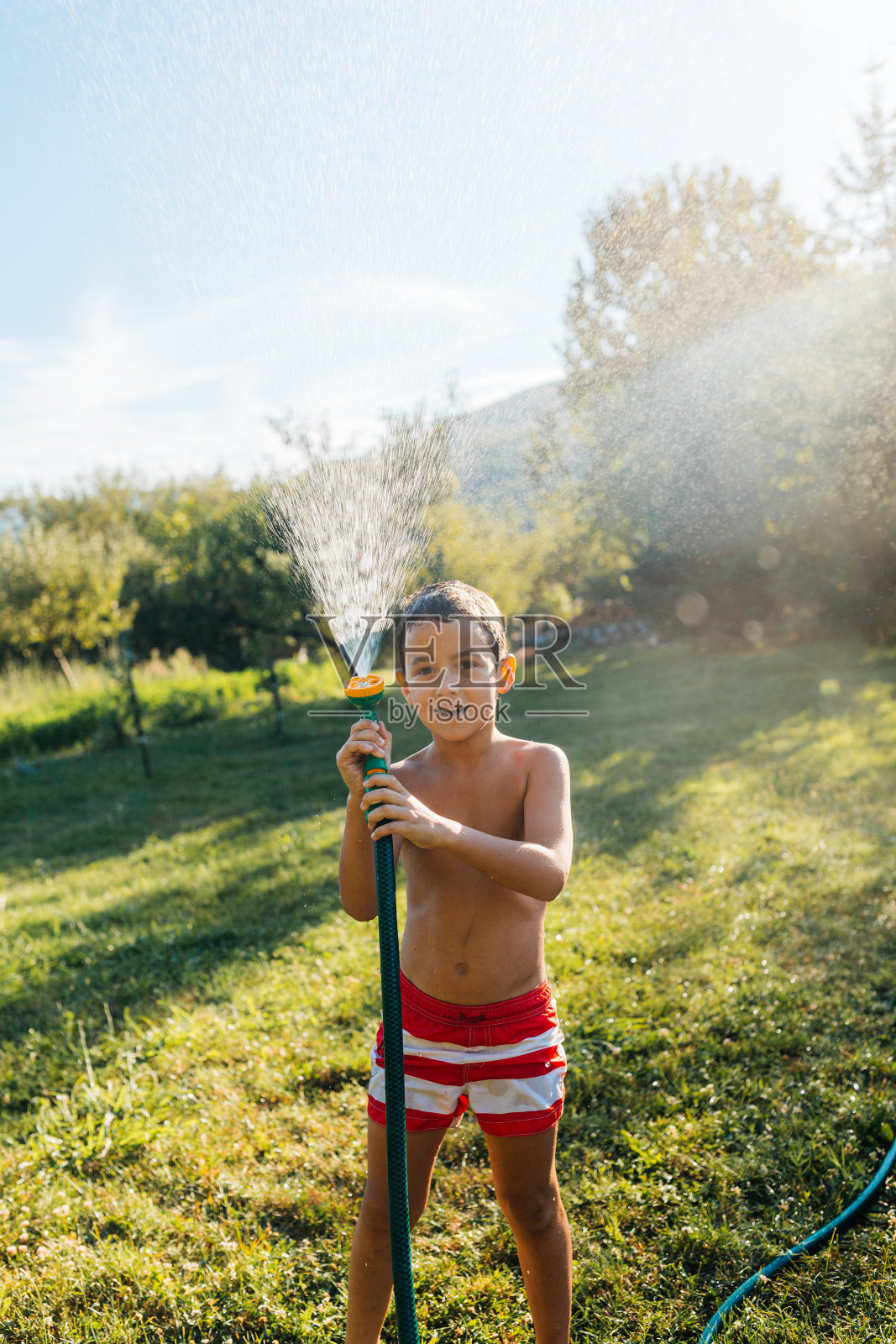 一个十几岁的男孩在炎热的夏日里用花园软管喷药照片摄影图片