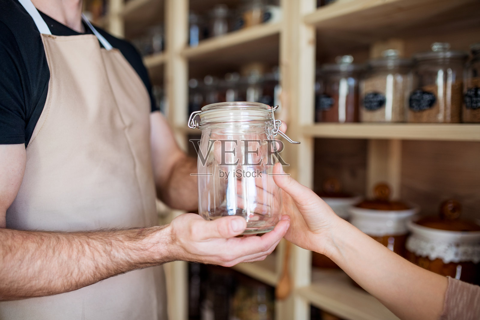 帅气的店员在无包装商店使用可重复使用的容器为顾客服务。零废物商店提供无包装散装商品和可持续替代品。照片摄影图片