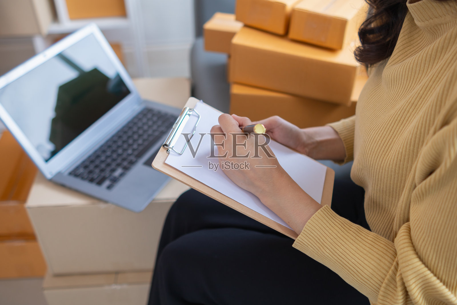 女商人决定在家里投资中小企业，使用笔记本电脑和智能手机进行在线营销，并通过应用程序在线销售，然后根据订单包装产品。照片摄影图片