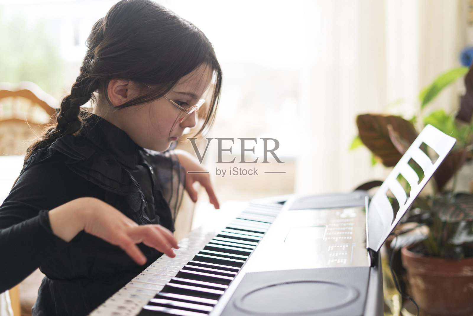 一个可爱的小女孩戴着眼镜，扎着辫子，穿着黑色的裙子在学弹钢琴。照片摄影图片