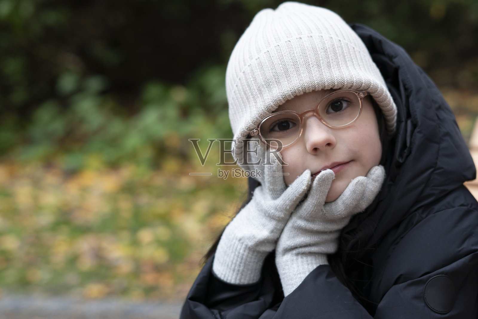 深秋，一个戴着眼镜和帽子的美丽的小女孩坐在公园的长凳上照片摄影图片