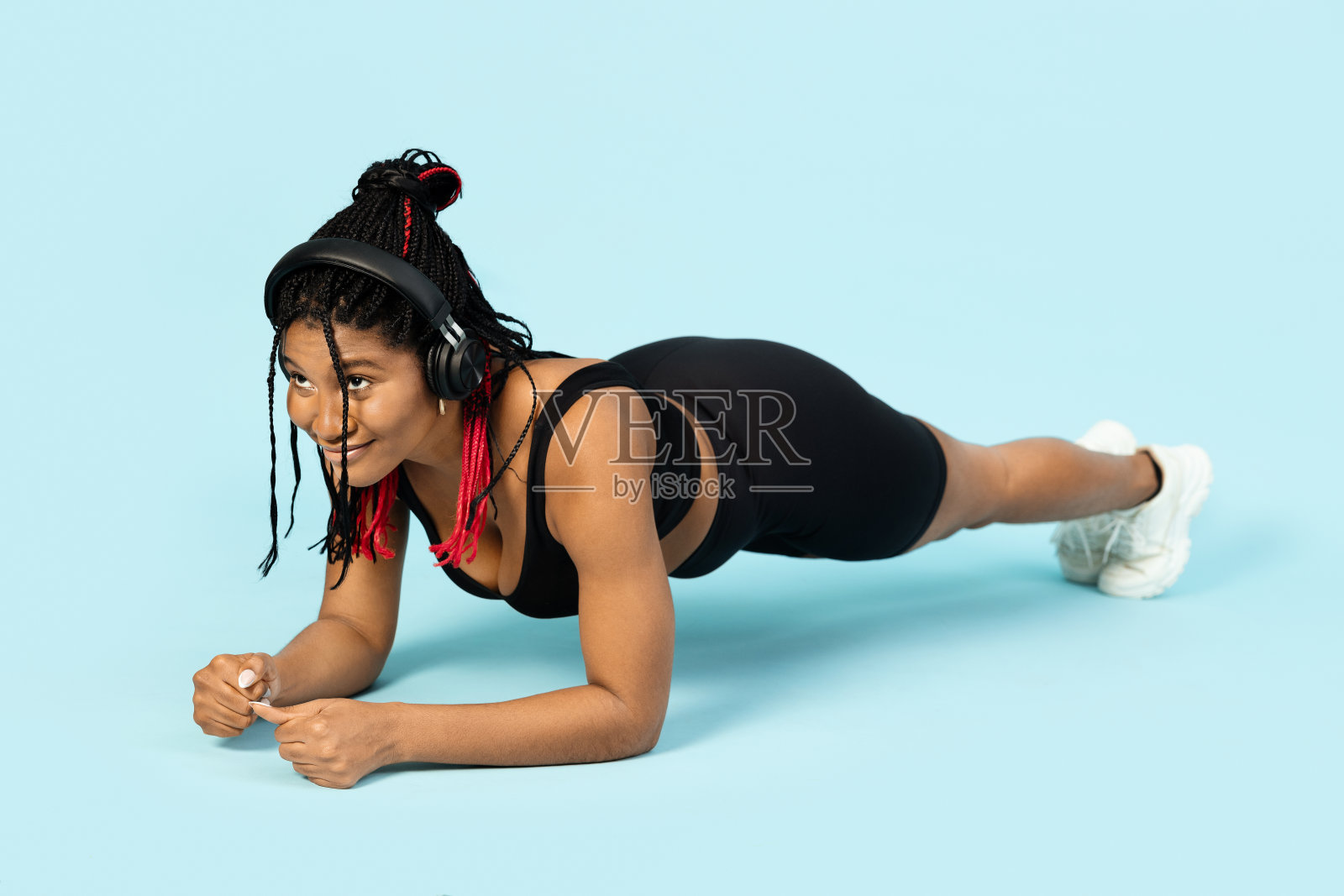 一个女人做平板支撑，听音乐，在蓝色的背景下享受锻炼。照片摄影图片