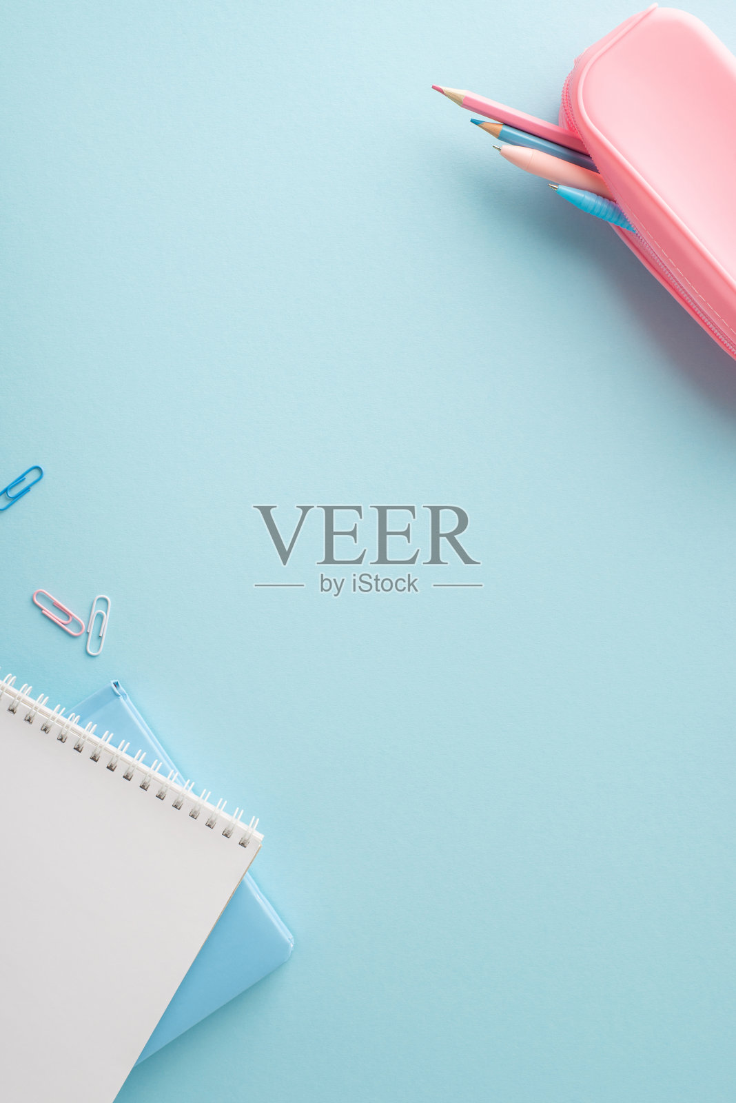 极简垂直的学校用品，有一个粉红色的铅笔盒，蓝色的笔记本，和蓝色背景的夹子照片摄影图片
