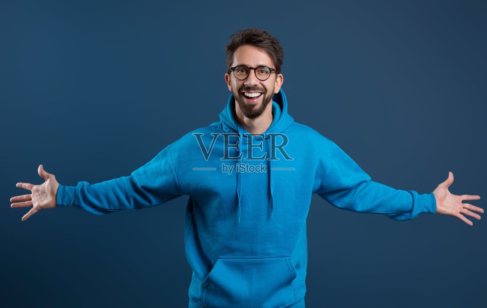 穿着蓝色连帽衫的开朗年轻人对着镜头张开双臂微笑照片摄影图片