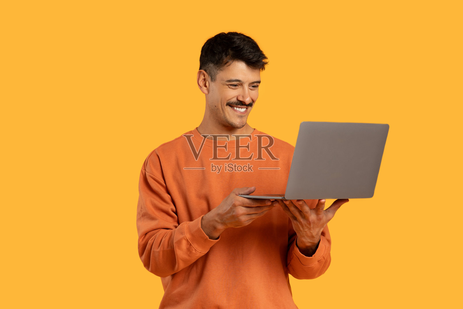 身穿橙色毛衣的男子手持黄色背景的笔记本电脑照片摄影图片