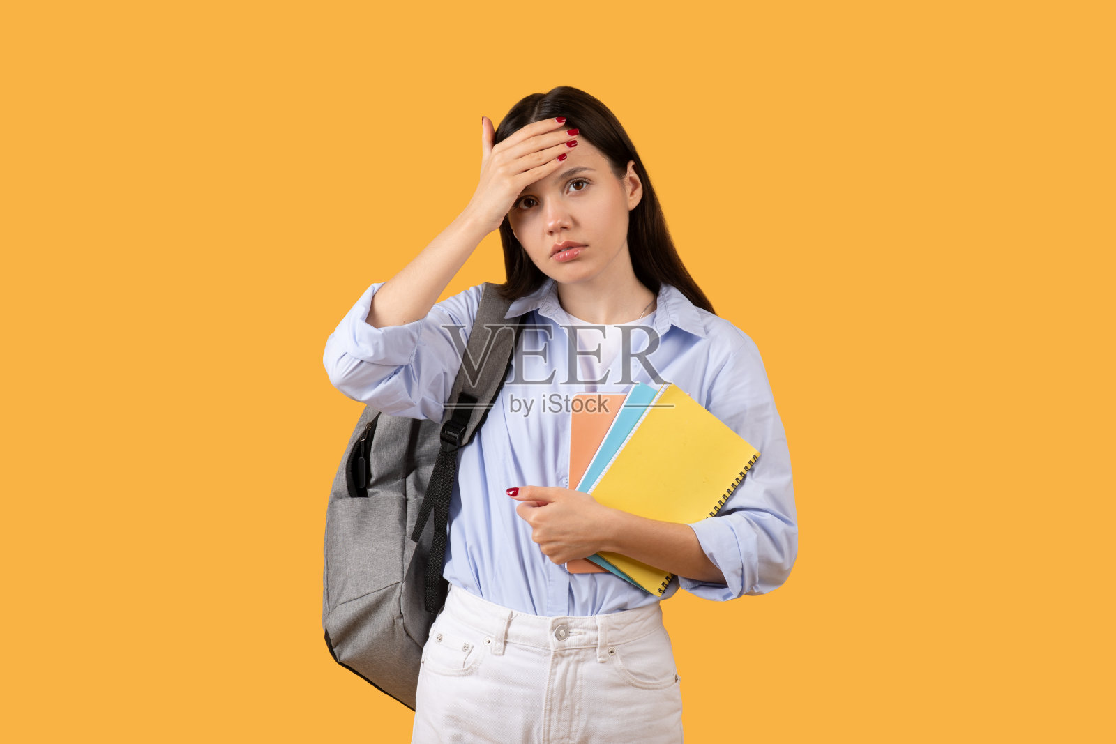 忧心忡忡的女学生背着双肩包，手里拿着笔记本，表现出紧张或困惑照片摄影图片