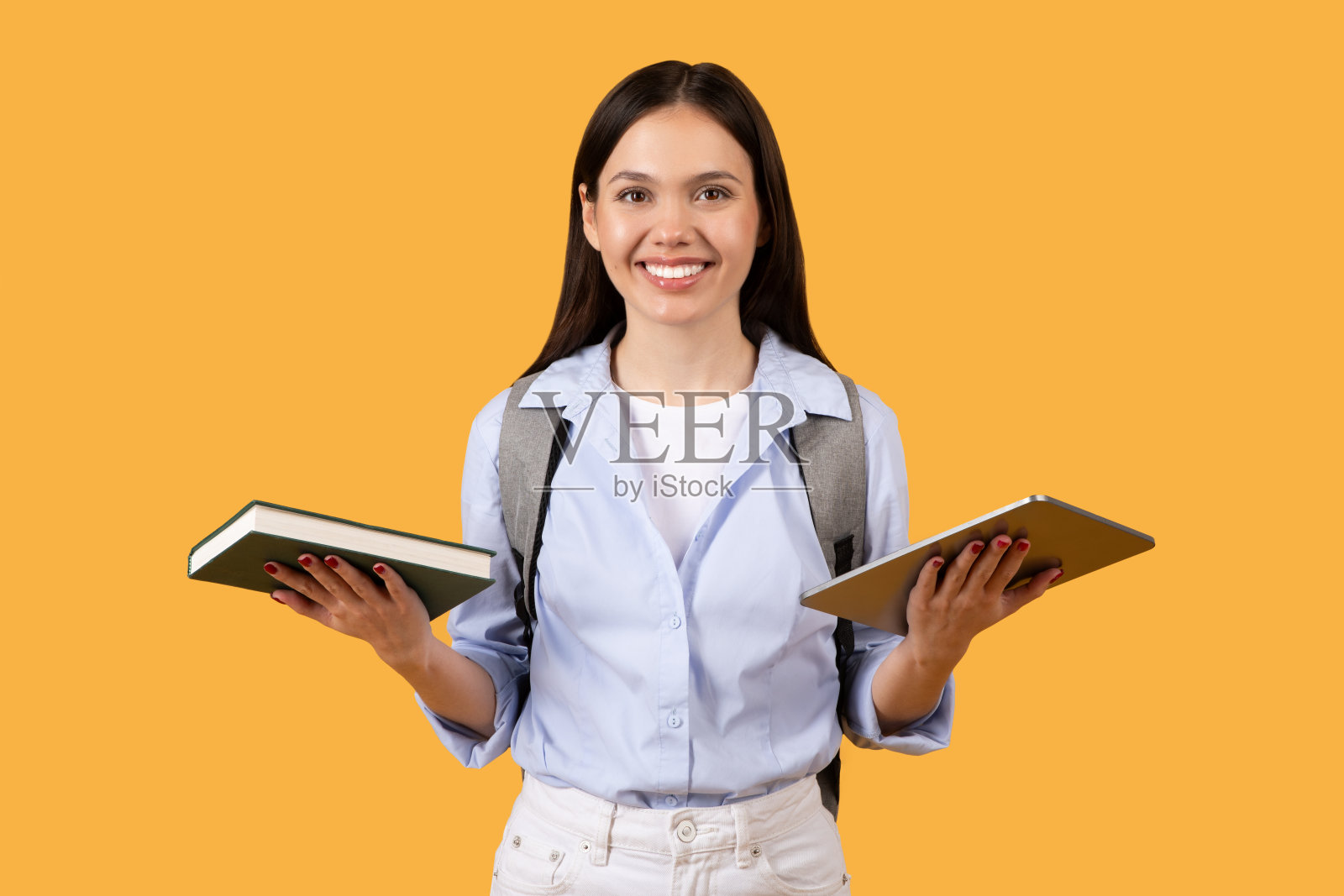 女学生在黄色背景下比较书和写字板照片摄影图片