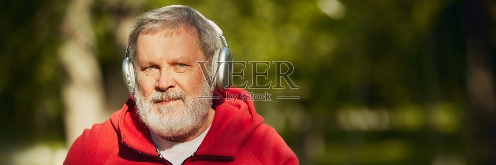 保持健康和快乐。在一个阳光明媚的早晨，一位老人戴着耳机在公园慢跑，展示了保持健康的乐趣。横幅照片摄影图片