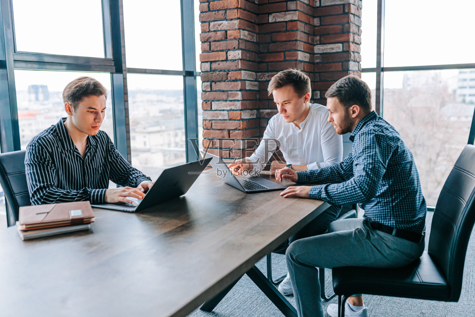 三个年轻人在公司办公室里通过笔记本电脑与他们的导师合作。照片摄影图片