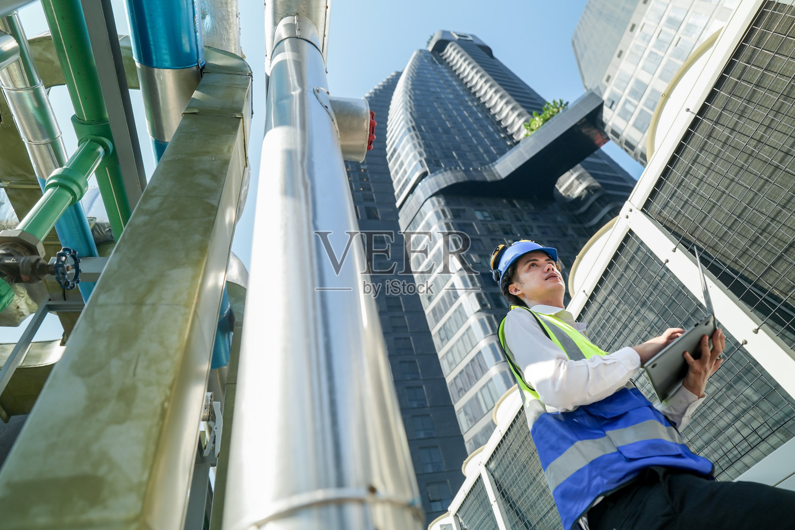 工业工程师在工地用无线电通讯调节管道阀门。城市建筑工地的工程师使用无线电与阳光明媚的工业屋顶上的团队协调。照片摄影图片