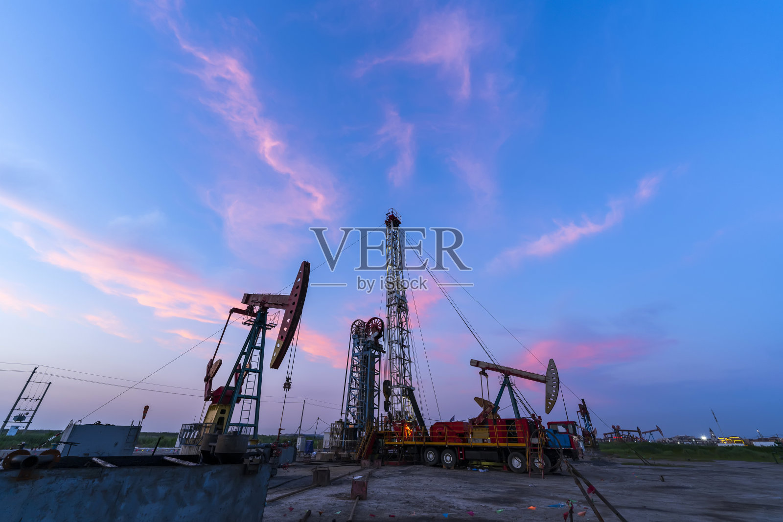 油田现场，傍晚，油泵都在运转，水泵和美丽的夕阳倒映在水面上照片摄影图片