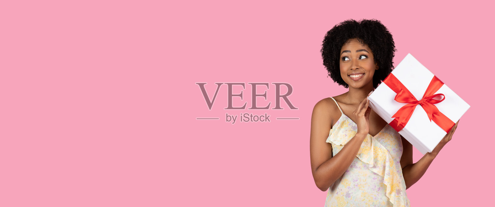 一个开朗的年轻女人，留着卷曲的非洲式头发，惊喜地拿着一个白色的大礼盒照片摄影图片