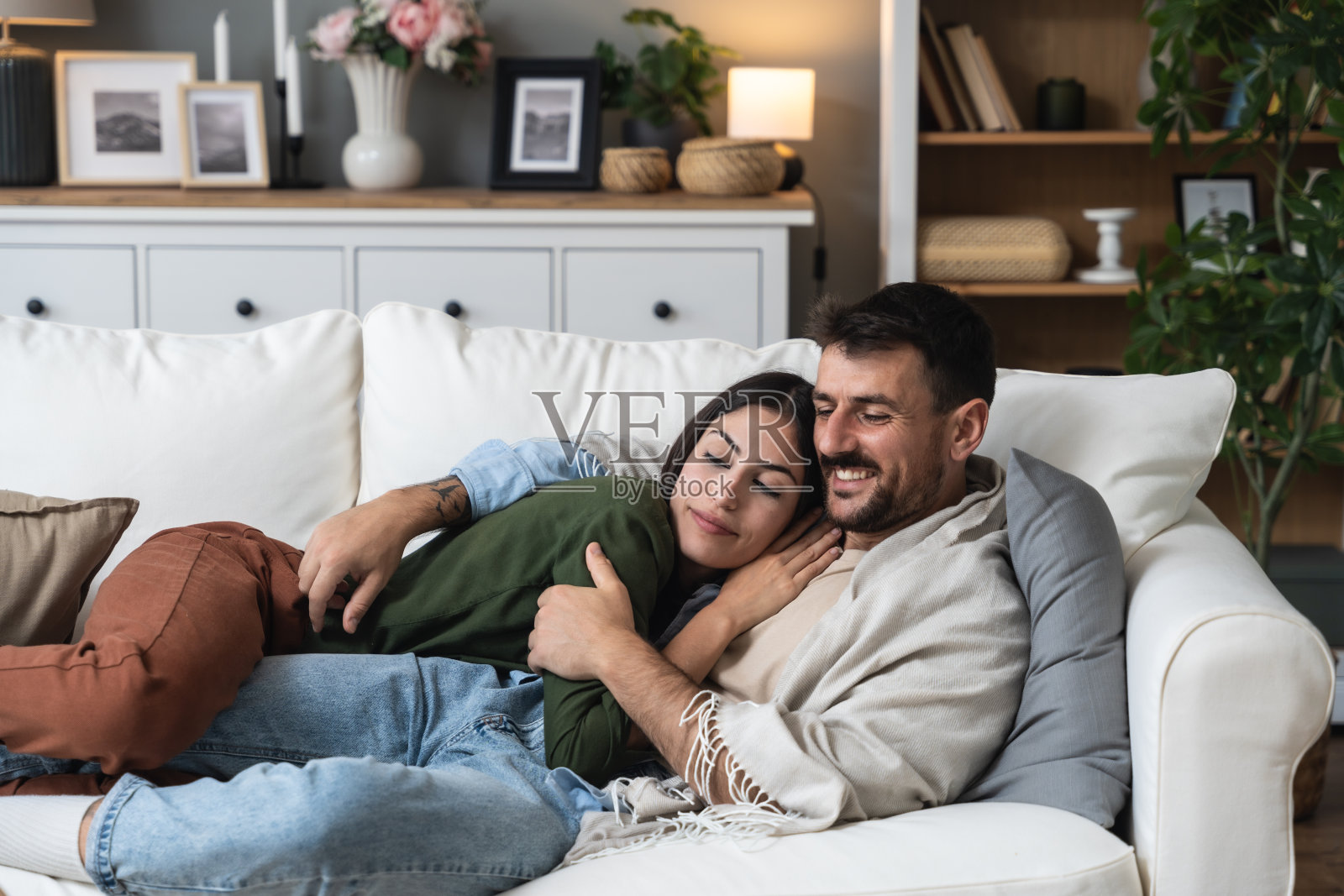 简单的生活，几个目标。年轻的男人和女人，刚刚结婚躺在沙发上拥抱在他们的新公寓。在辛苦工作后休息的情侣，享受周末的活动。照片摄影图片
