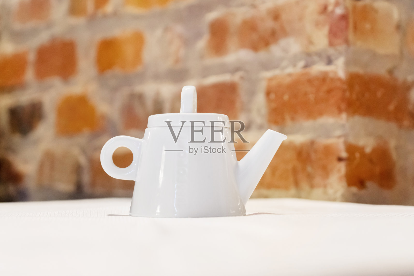 桌子上的白色茶壶，砖墙背景照片摄影图片