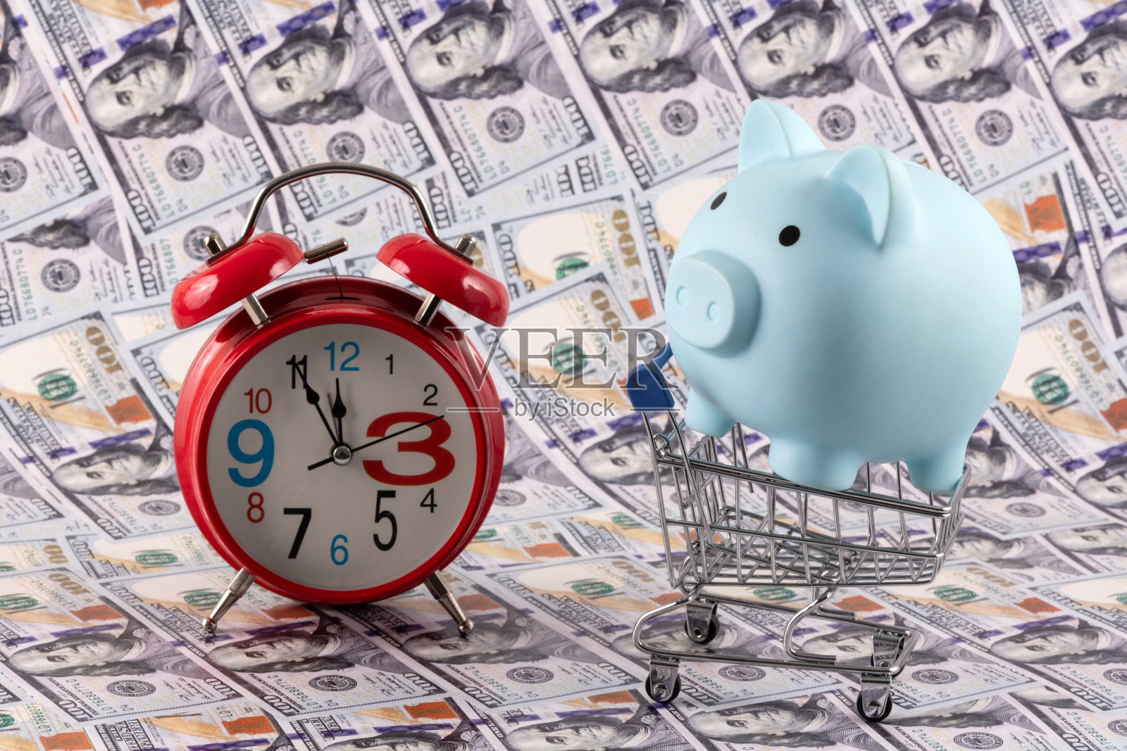 以100美元为背景的储蓄罐、超市购物车和闹钟照片摄影图片