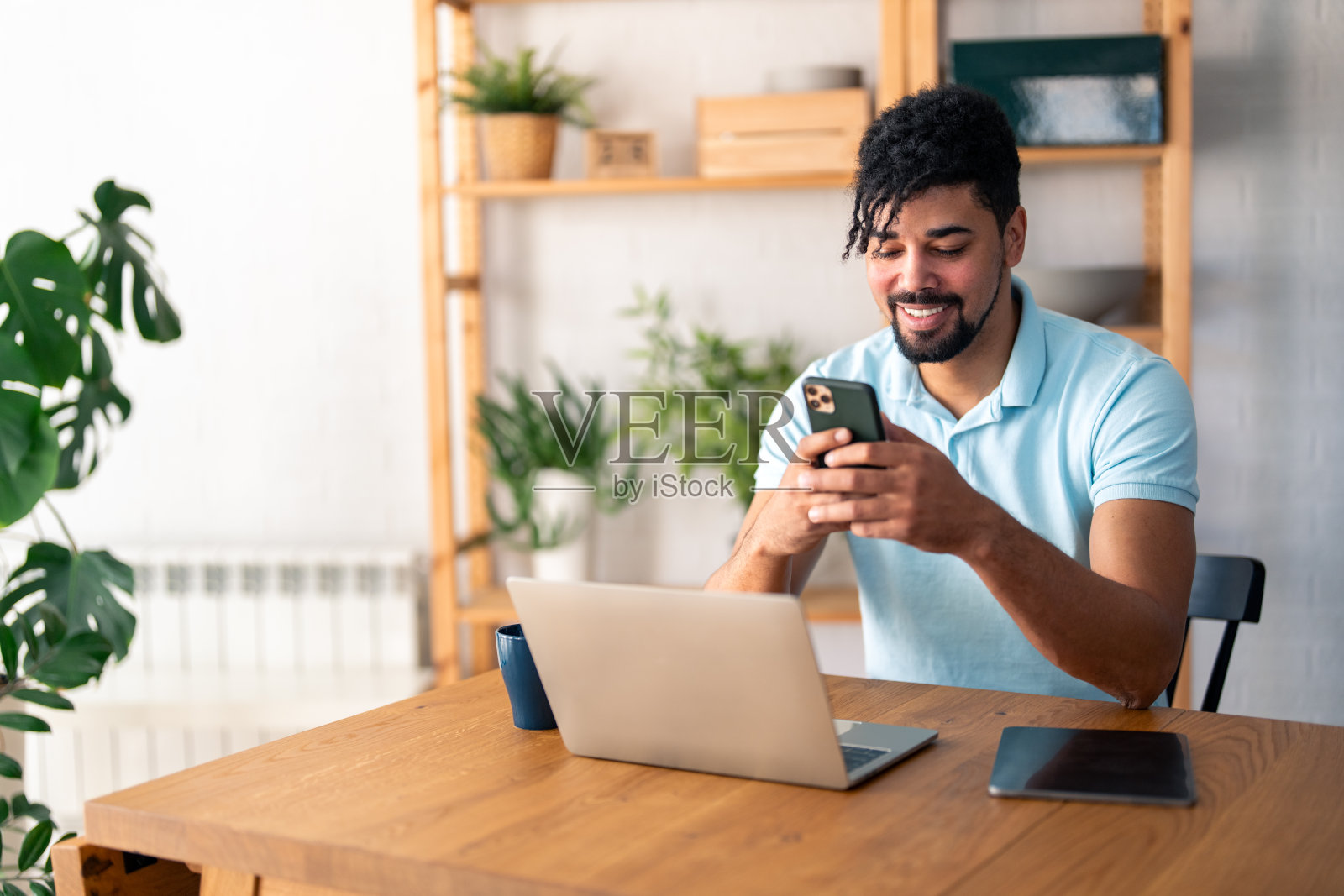 快乐微笑的商人穿着休闲的衣服，在他的家庭办公室使用现代智能手机照片摄影图片