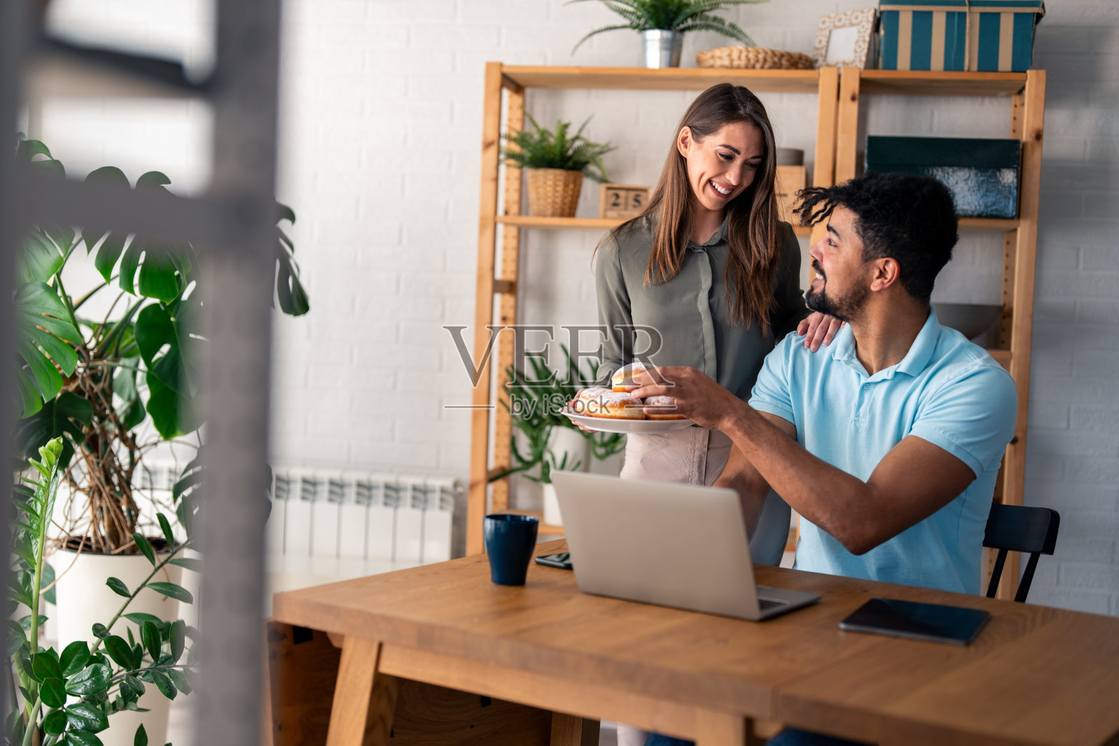 当丈夫在笔记本电脑上努力工作时，支持丈夫的妻子会给他带甜甜圈照片摄影图片