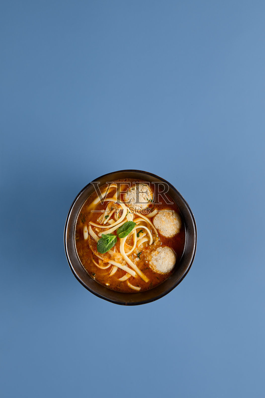 美味的鸡汤，肉丸和面条在黑色碗在蓝色背景照片摄影图片