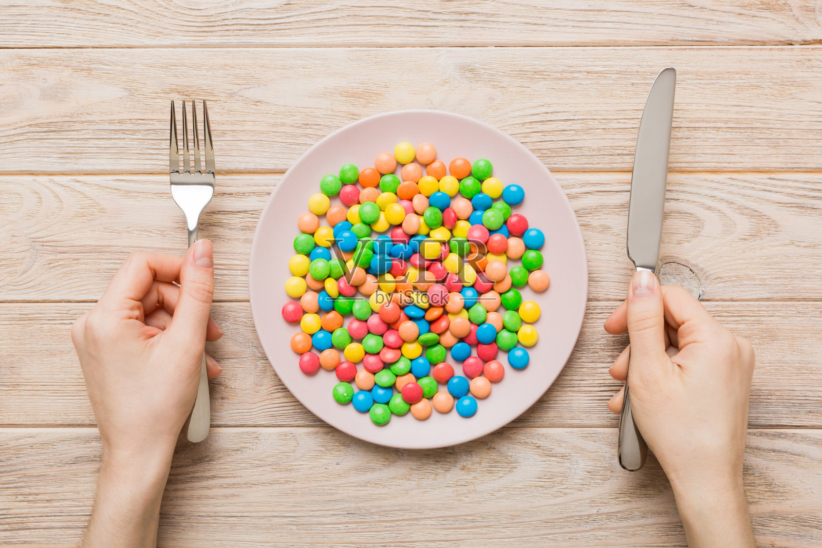 这个女孩手里拿着餐具，吃着盘子里的糖果。健康与肥胖概念，彩色背景俯视图照片摄影图片