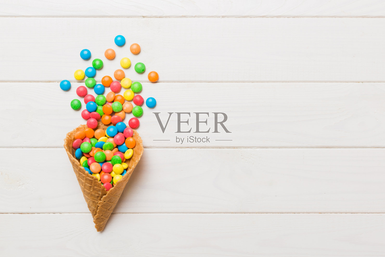 华夫蛋筒充满了各种传统糖果落在彩色背景与复制空间。快乐假期销售概念照片摄影图片