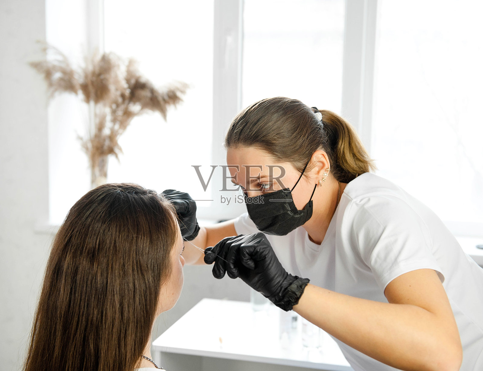 布朗斯特用镊子矫正眉毛。一个深色头发的模特在灯光工作室里坐在修眉师那里做眉毛矫正。照片摄影图片