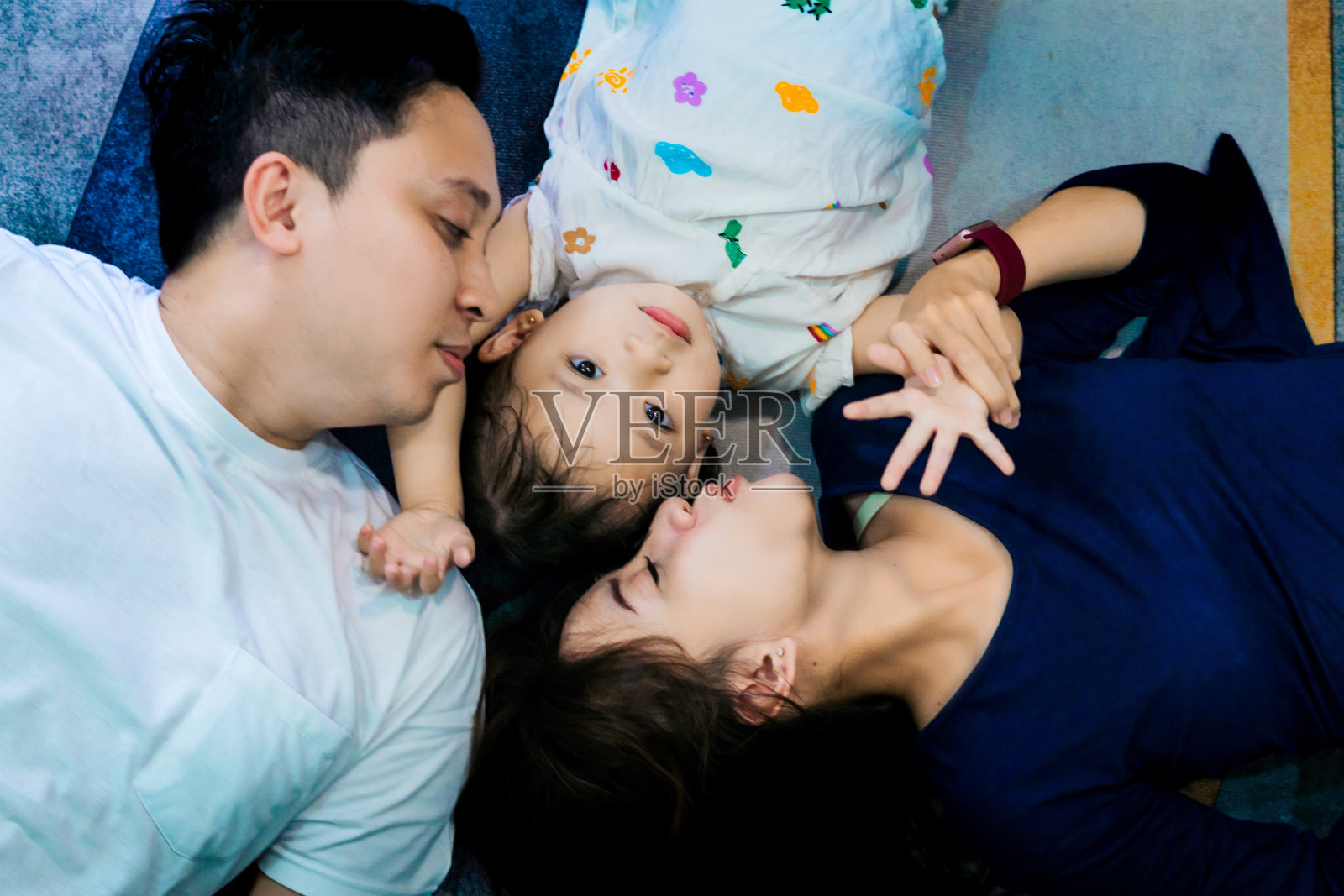 一个小家庭躺在客厅的蓝色地毯上，看起来很开心照片摄影图片