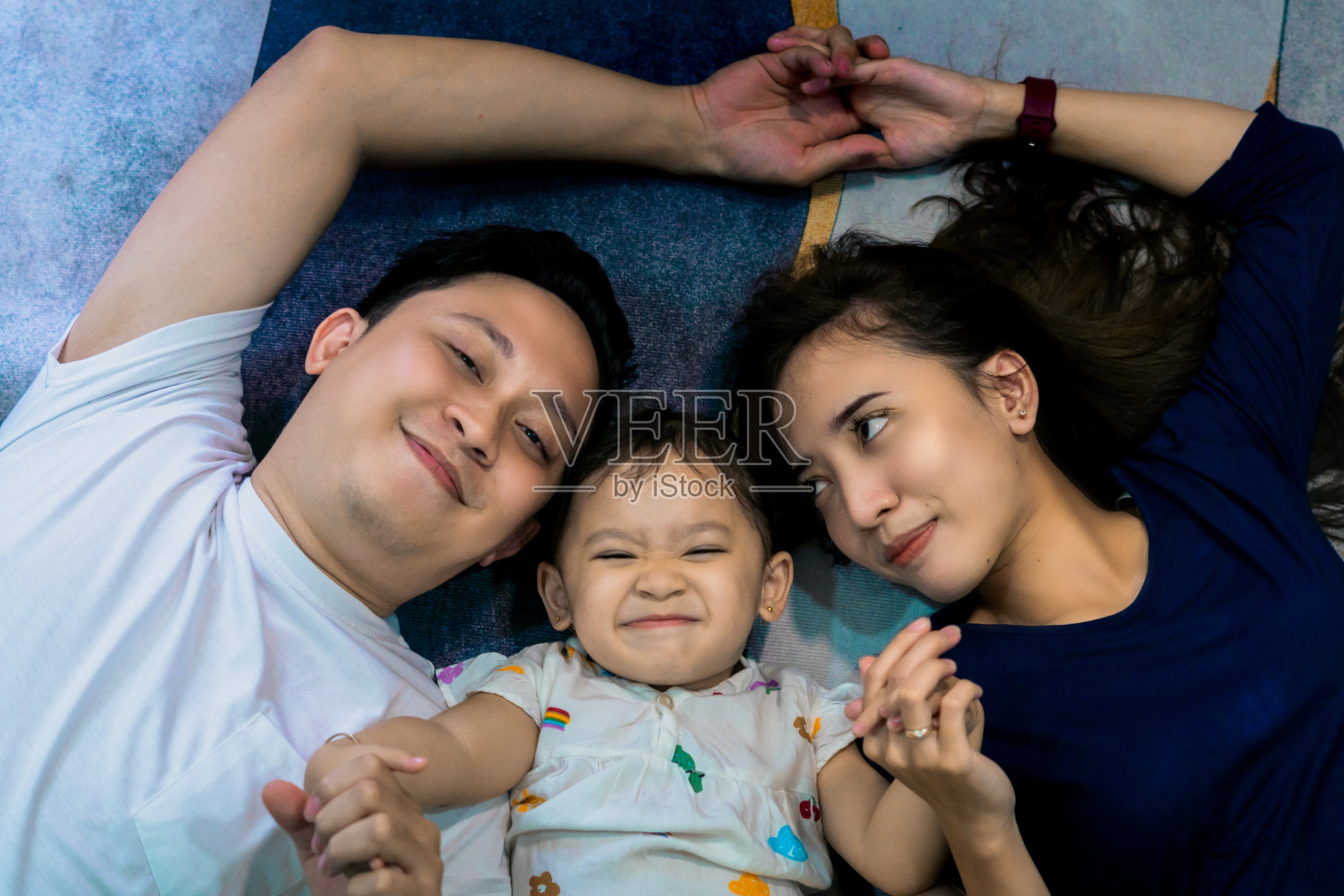 一个小家庭躺在客厅的蓝色地毯上，看起来很开心照片摄影图片