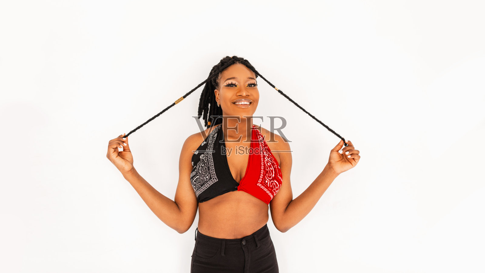 积极的年轻非洲女子，带着快乐的微笑，戴着时髦的红黑头巾，在白色背景下摆姿势。可爱的微笑的非洲裔美国女孩模特穿着时髦的衣服。现代时尚。照片摄影图片